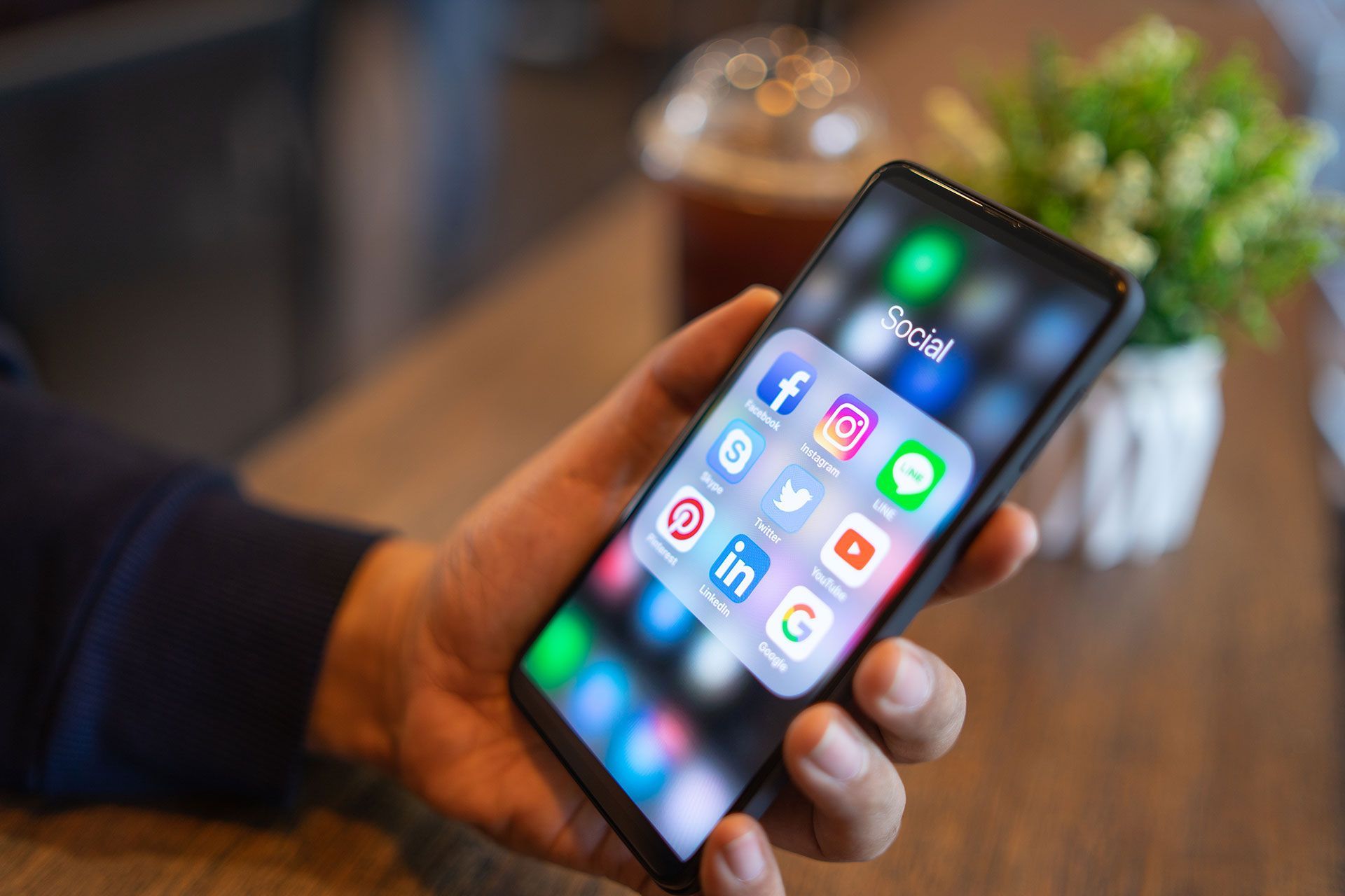 A person is holding a cell phone with social media icons on the screen.