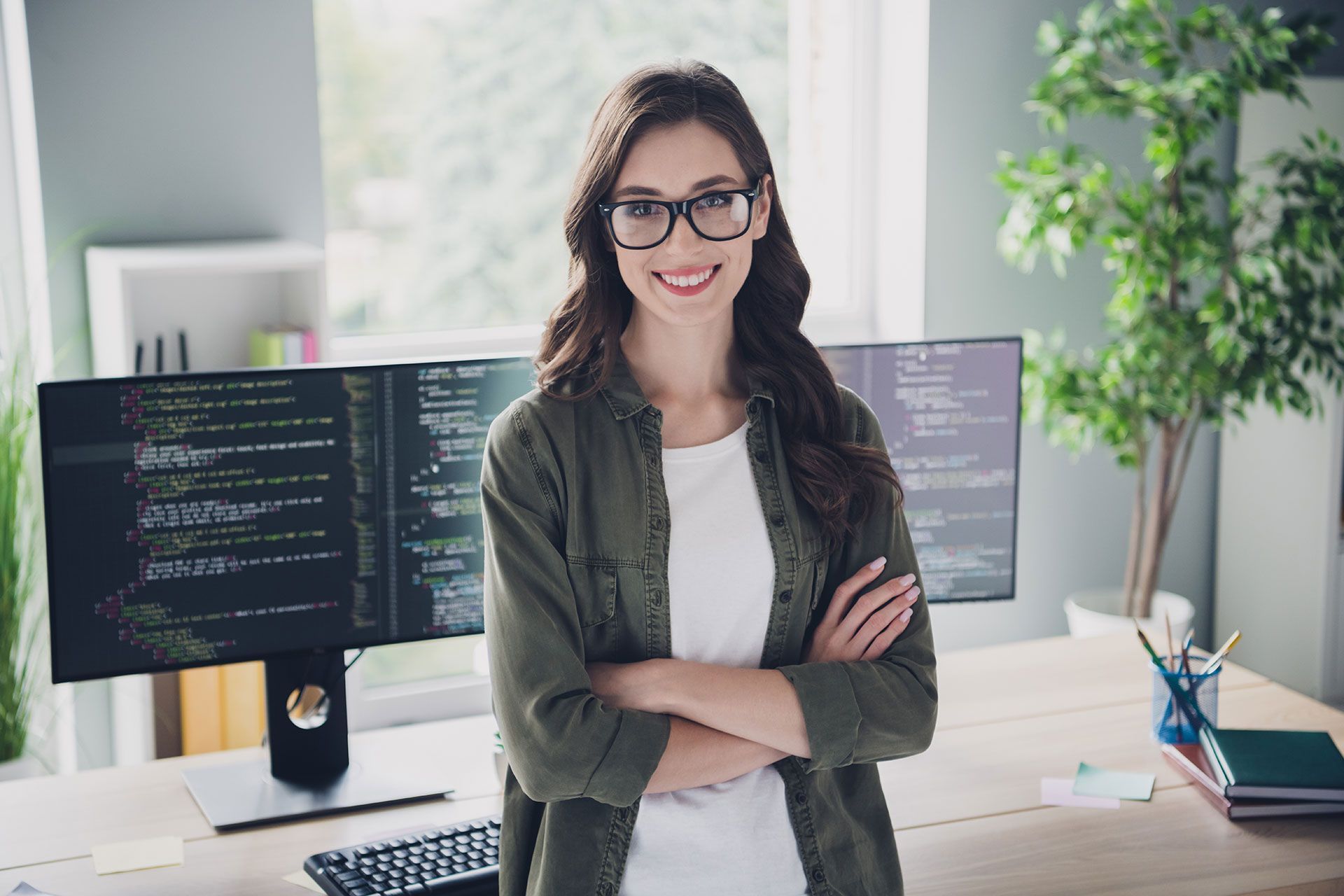 A woman is standing in front of a computer with her arms crossed.