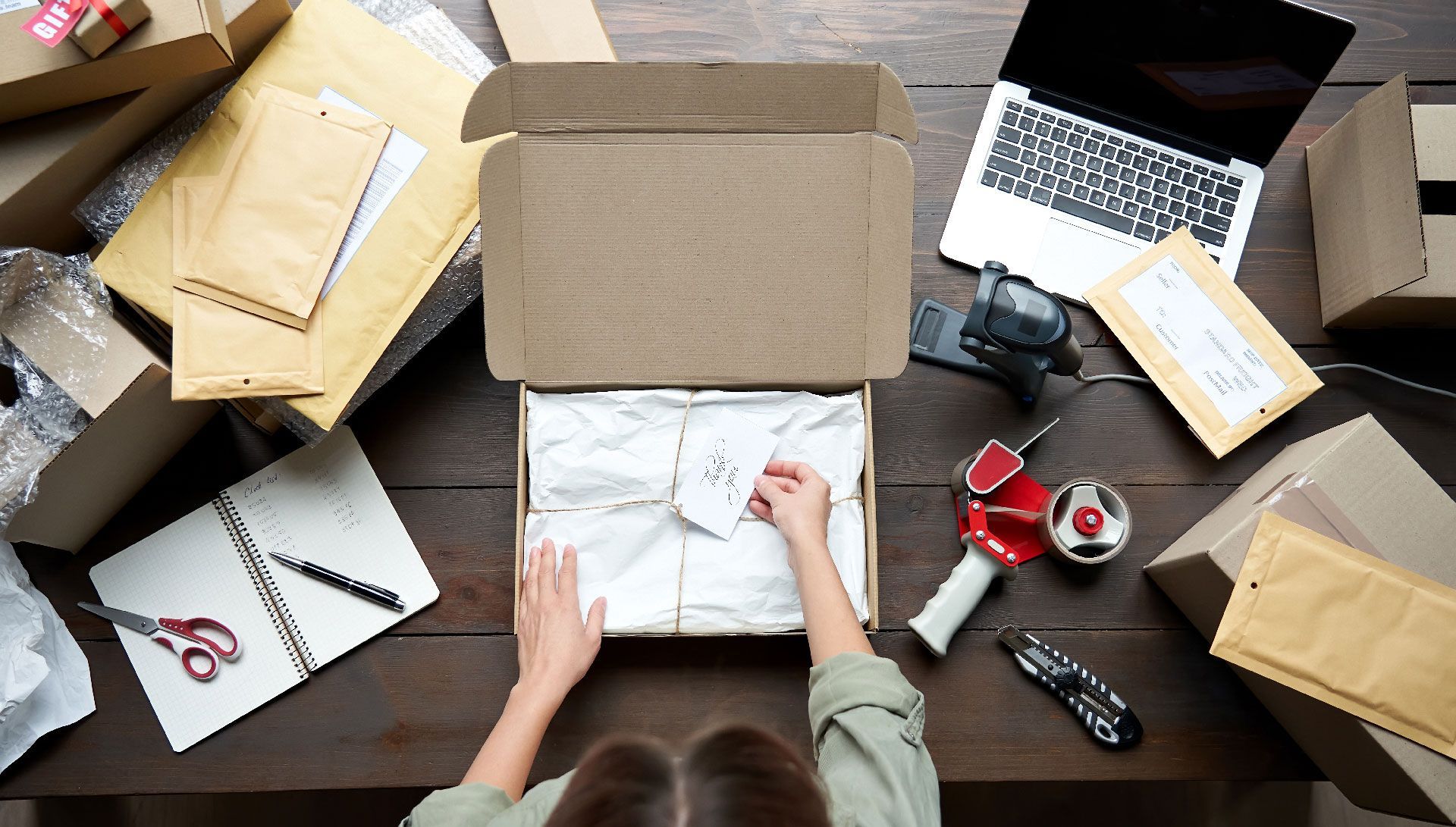 A woman is sitting at a table packing a box.