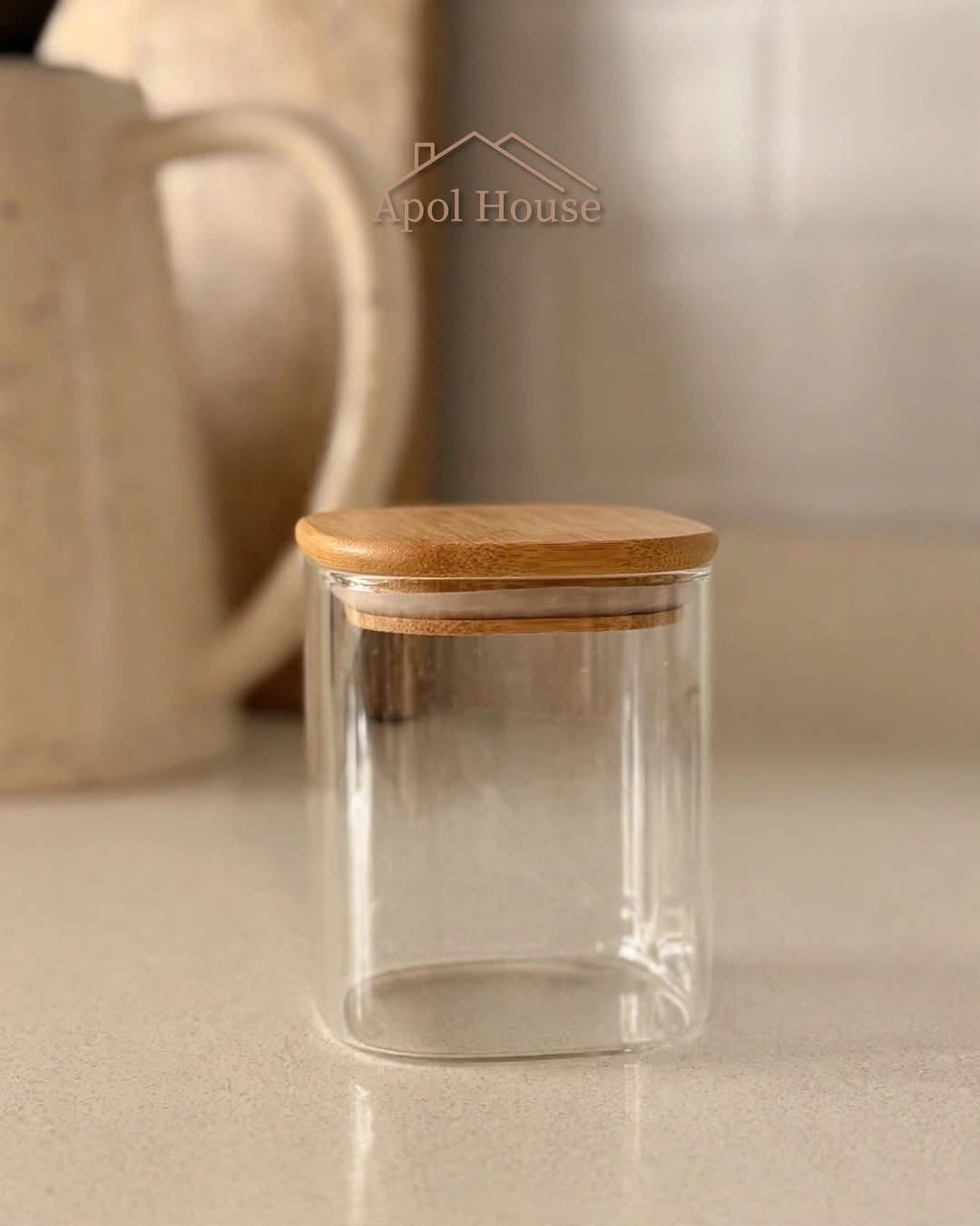 Tarro de vidrio transparente con tapa de madera sobre una encimera beige.