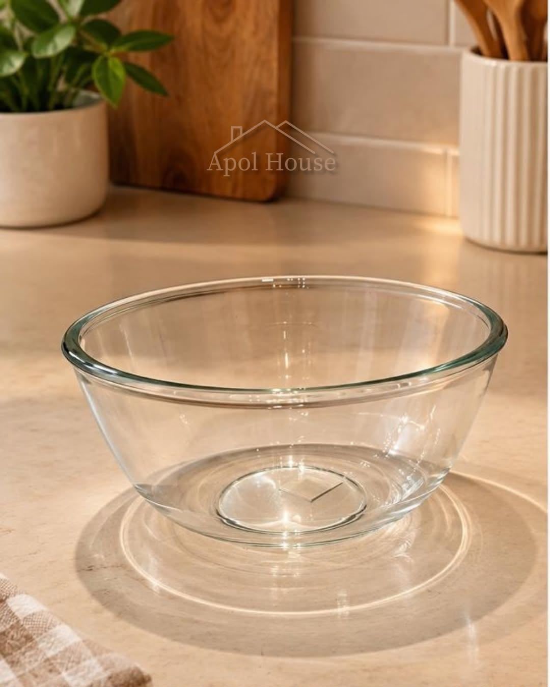 Un cuenco de cristal transparente sobre una encimera de madera, con plantas en macetas al fondo.