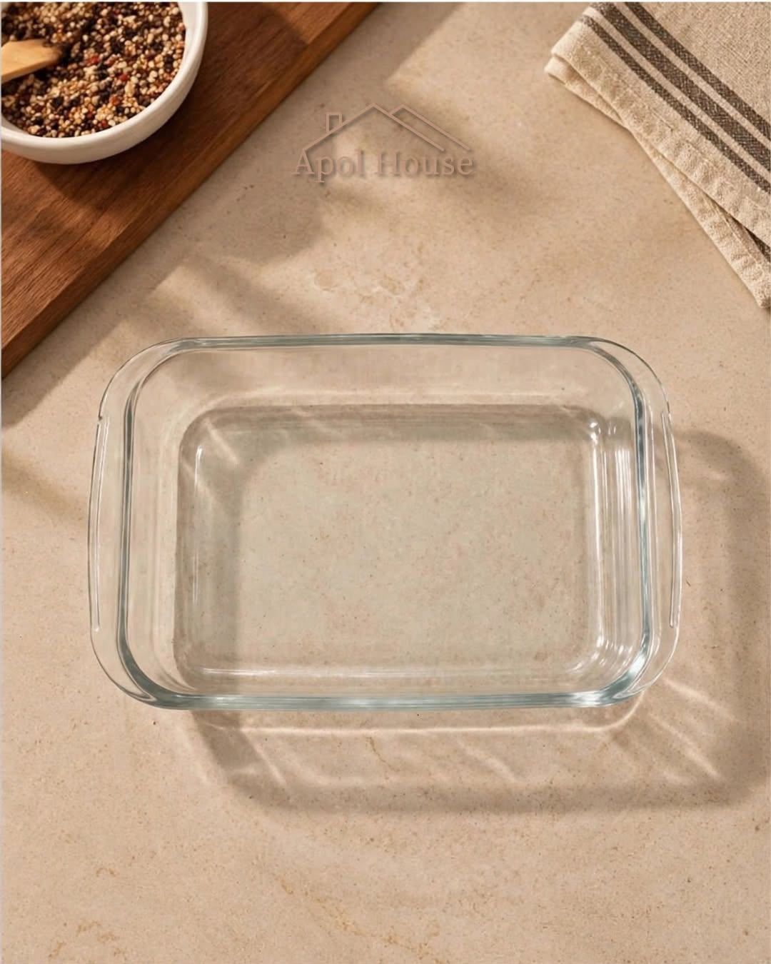 Una fuente rectangular de vidrio vacía sobre un paño beige, con una cuchara y un cuenco de especias cerca