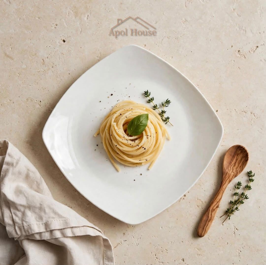 Plato cuadrado blanco con un nido de pasta y una guarnición de albahaca sobre una mesa beige, con una cuchara de madera cerca