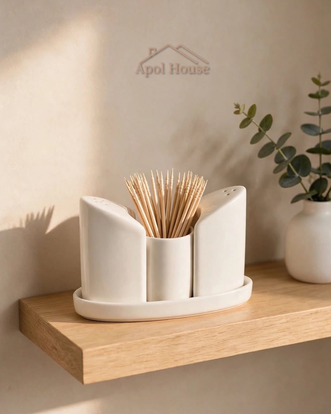 Portapalillos de cerámica blanca sobre un estante de madera junto a una planta, con «Apol House» en la pared del fondo.