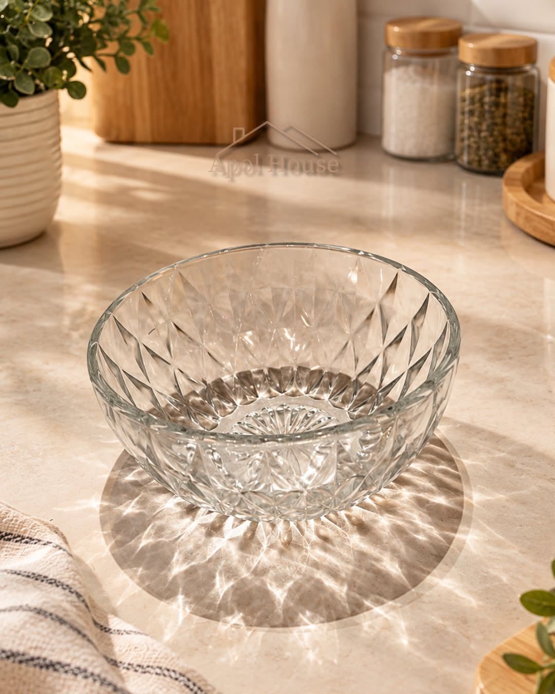 Un cuenco de vidrio transparente sobre una encimera de cocina iluminada por el sol, con tarros de especias al fondo