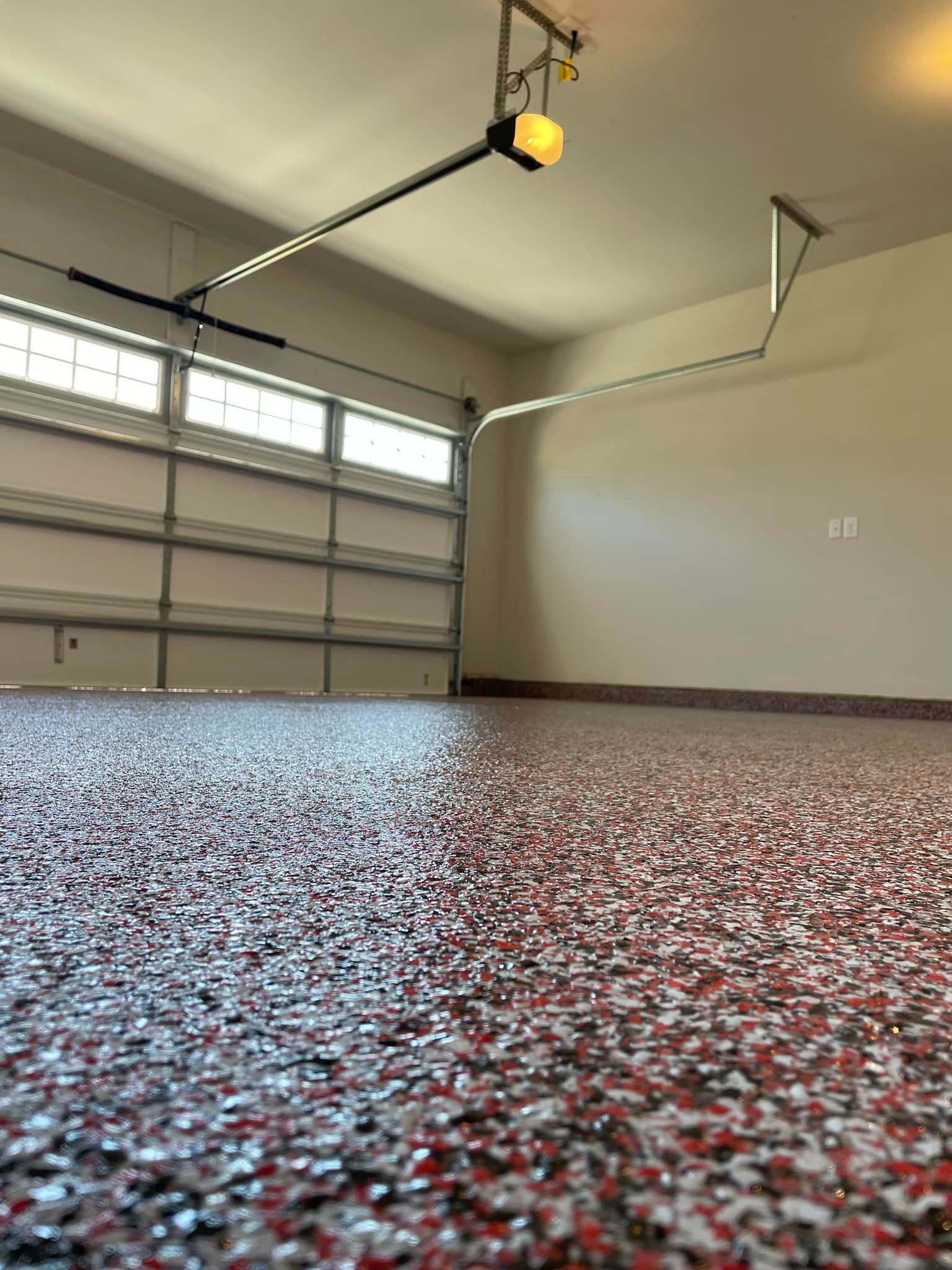 Garage interior with epoxy floor, open door, light beige walls, and overhead garage door opener.