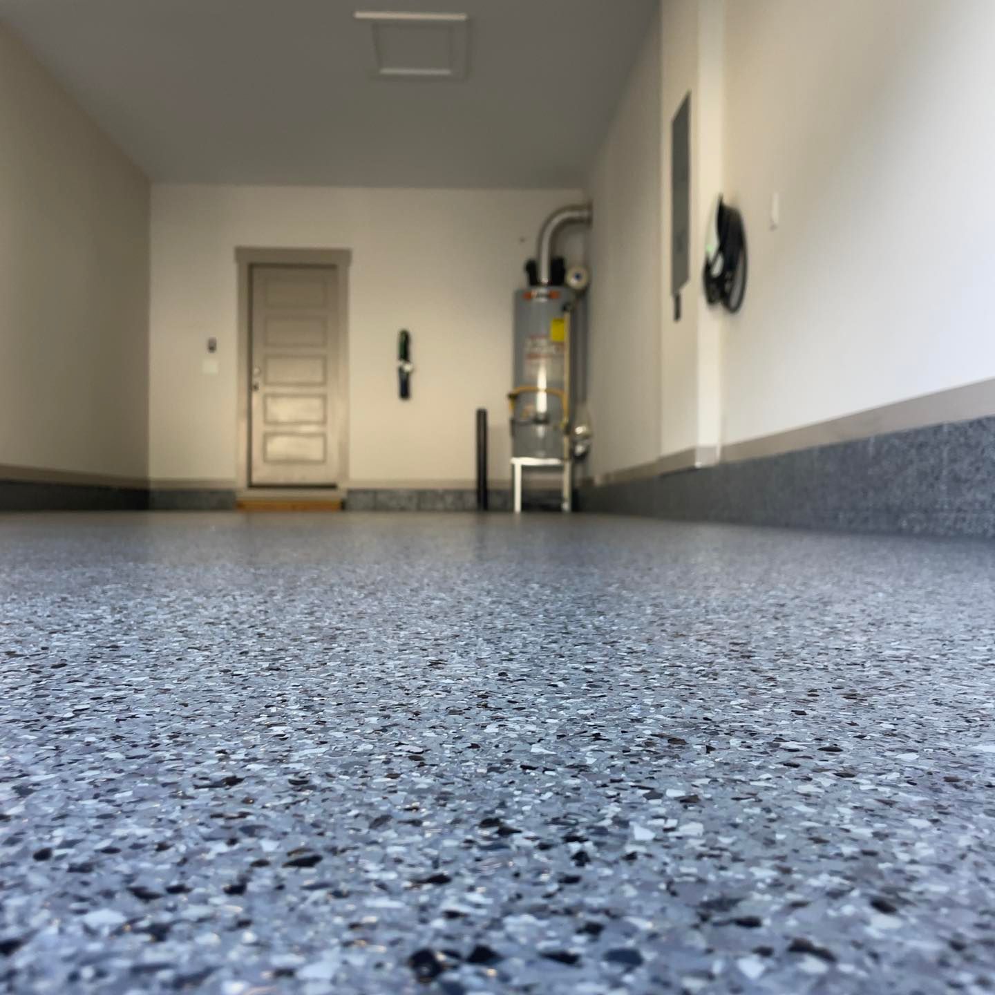Garage interior with gray speckled epoxy floor, white walls, and a door at the back.