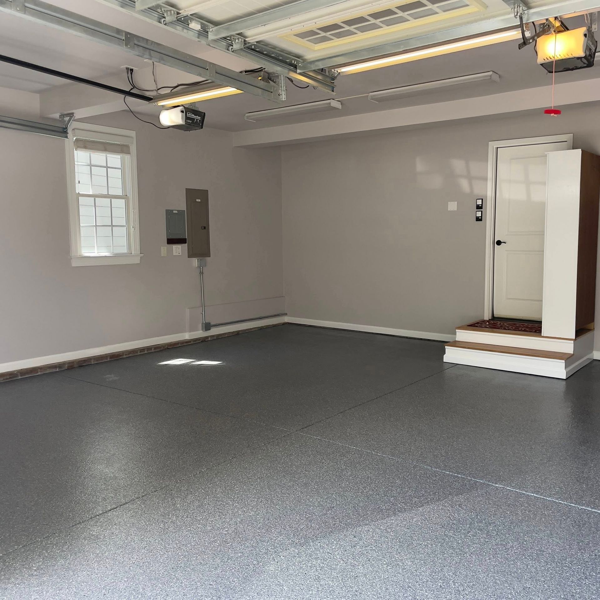Empty garage with epoxy floor, a door, a window, and overhead lighting.