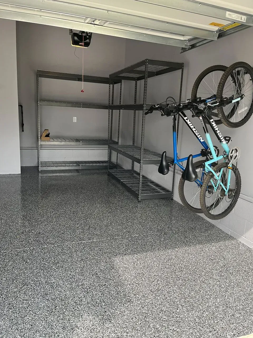 Garage interior with epoxy floor, metal shelving, and two bicycles mounted on a wall.