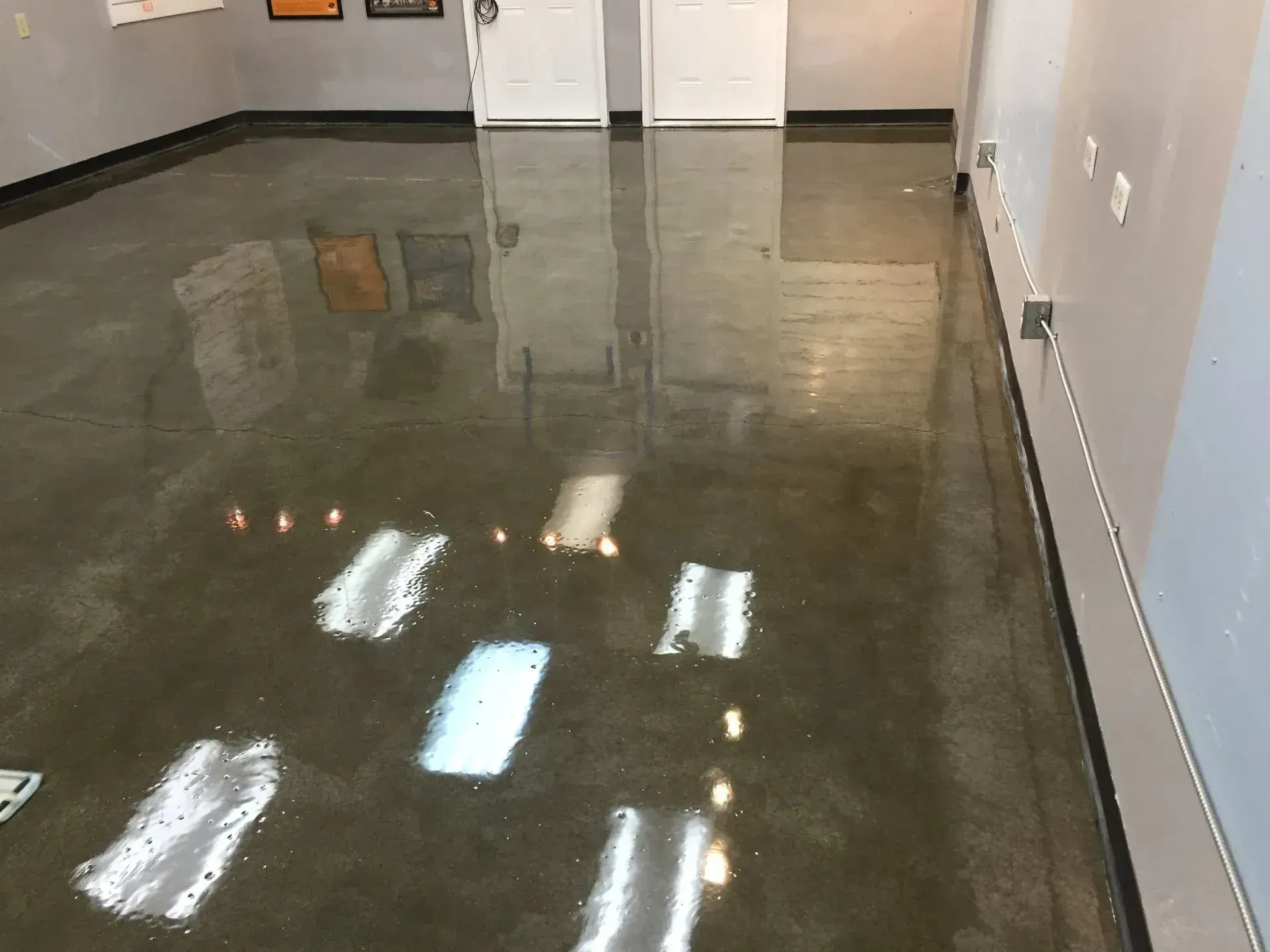 Shiny, concrete floor in a room with white walls and doorways. Light reflects off the surface.