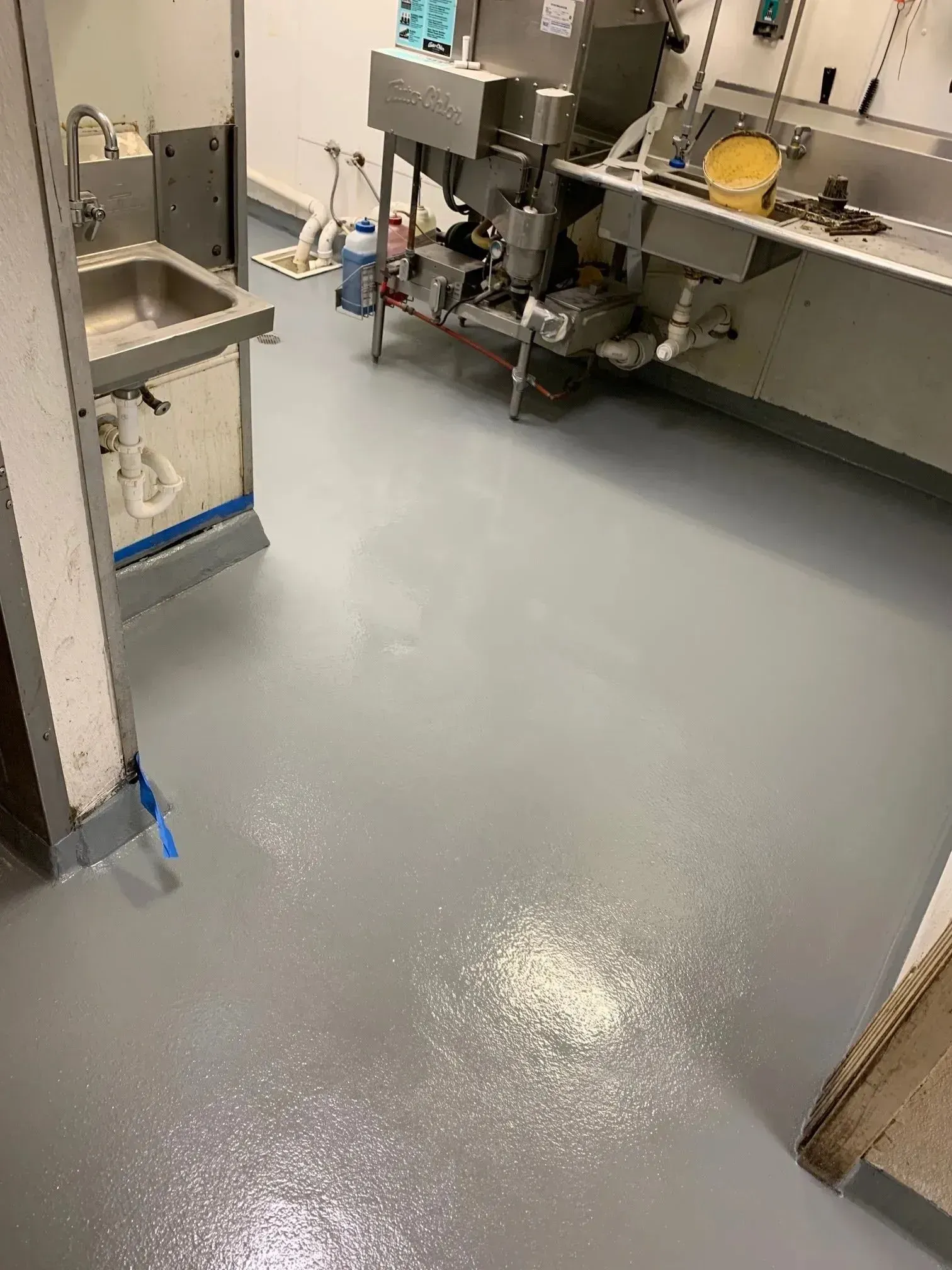 A gray-floored commercial kitchen with stainless steel equipment. White powder is scattered on the floor.