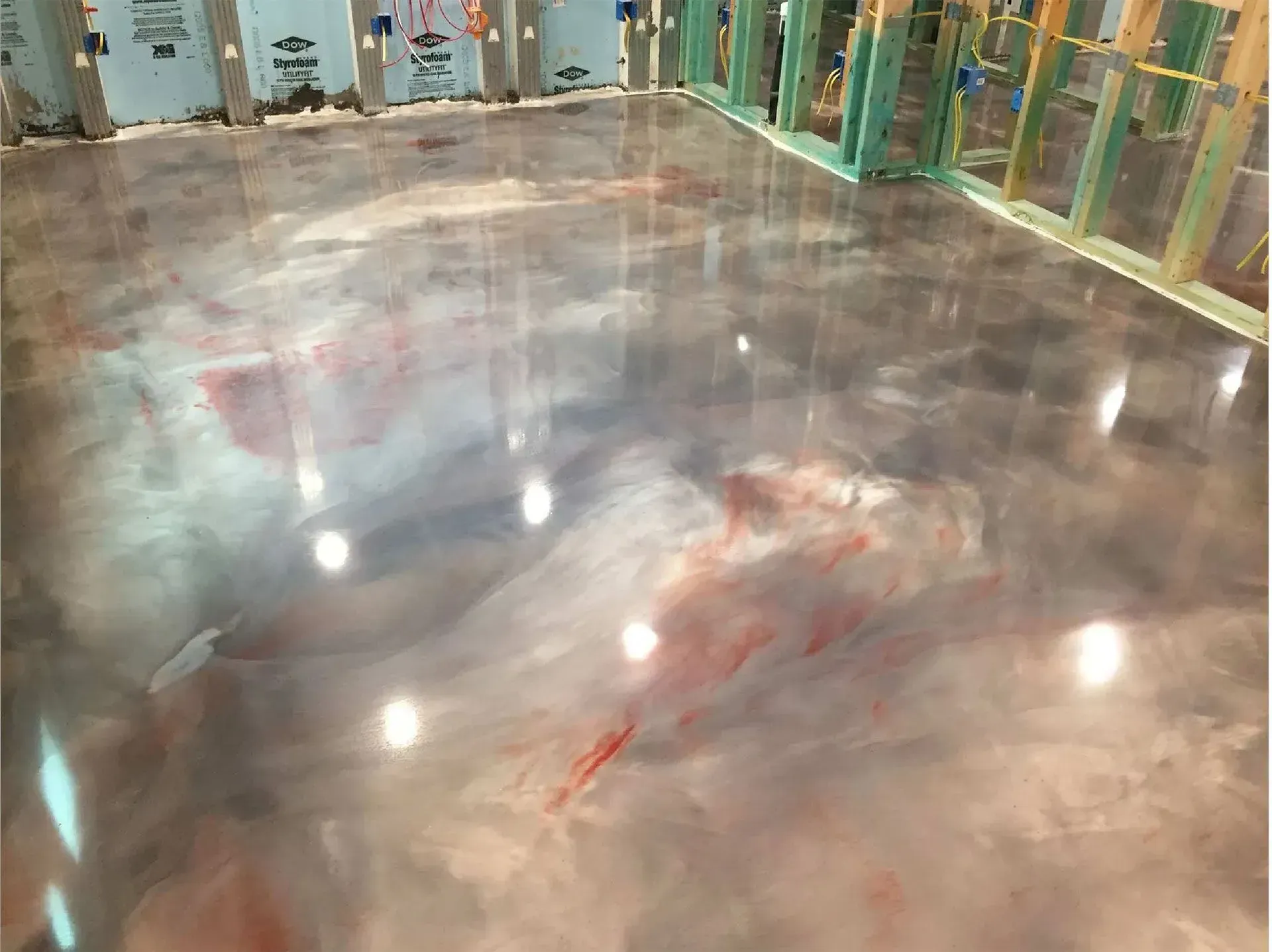 Metallic epoxy floor with swirled silver, gray, and red pigments, reflecting lights, in a construction space.