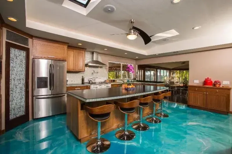 Kitchen with blue epoxy floor, wooden cabinets, stainless steel appliances, and a central island with bar stools.