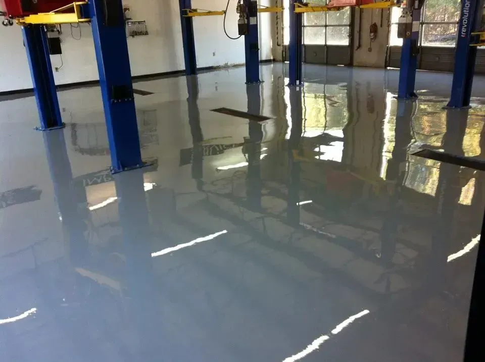 Gray epoxy floor reflecting a car repair shop's blue lifts and windows.