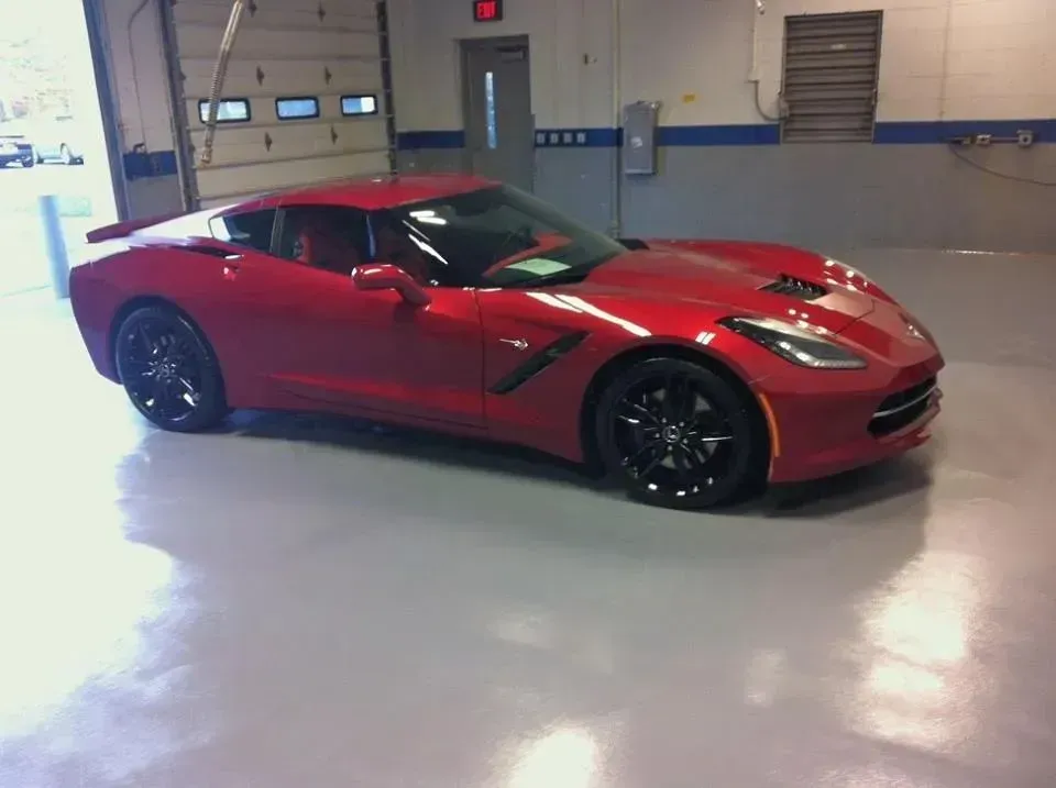 Red Corvette sports car parked indoors on a shiny, gray floor.