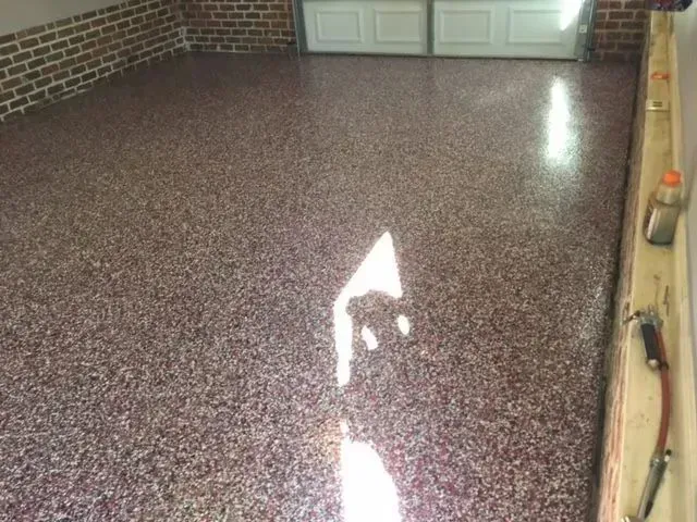 Garage floor with red and brown speckled epoxy coating. Brick wall on the left, garage door in the background.