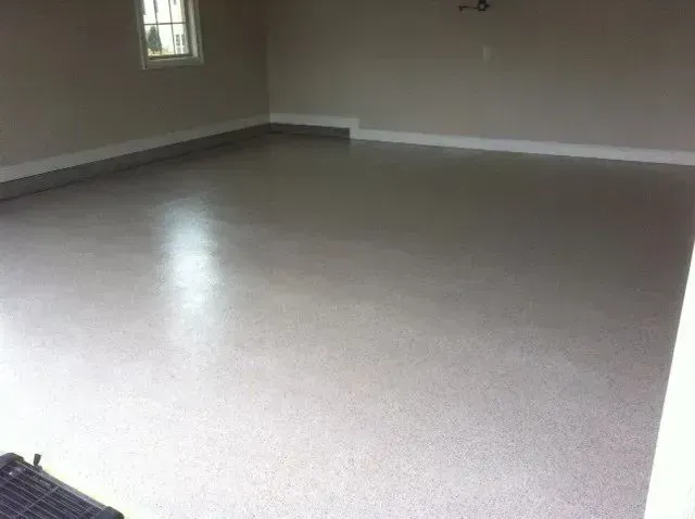 A newly painted, light gray garage floor. Empty space, white trim, and a small window are visible.