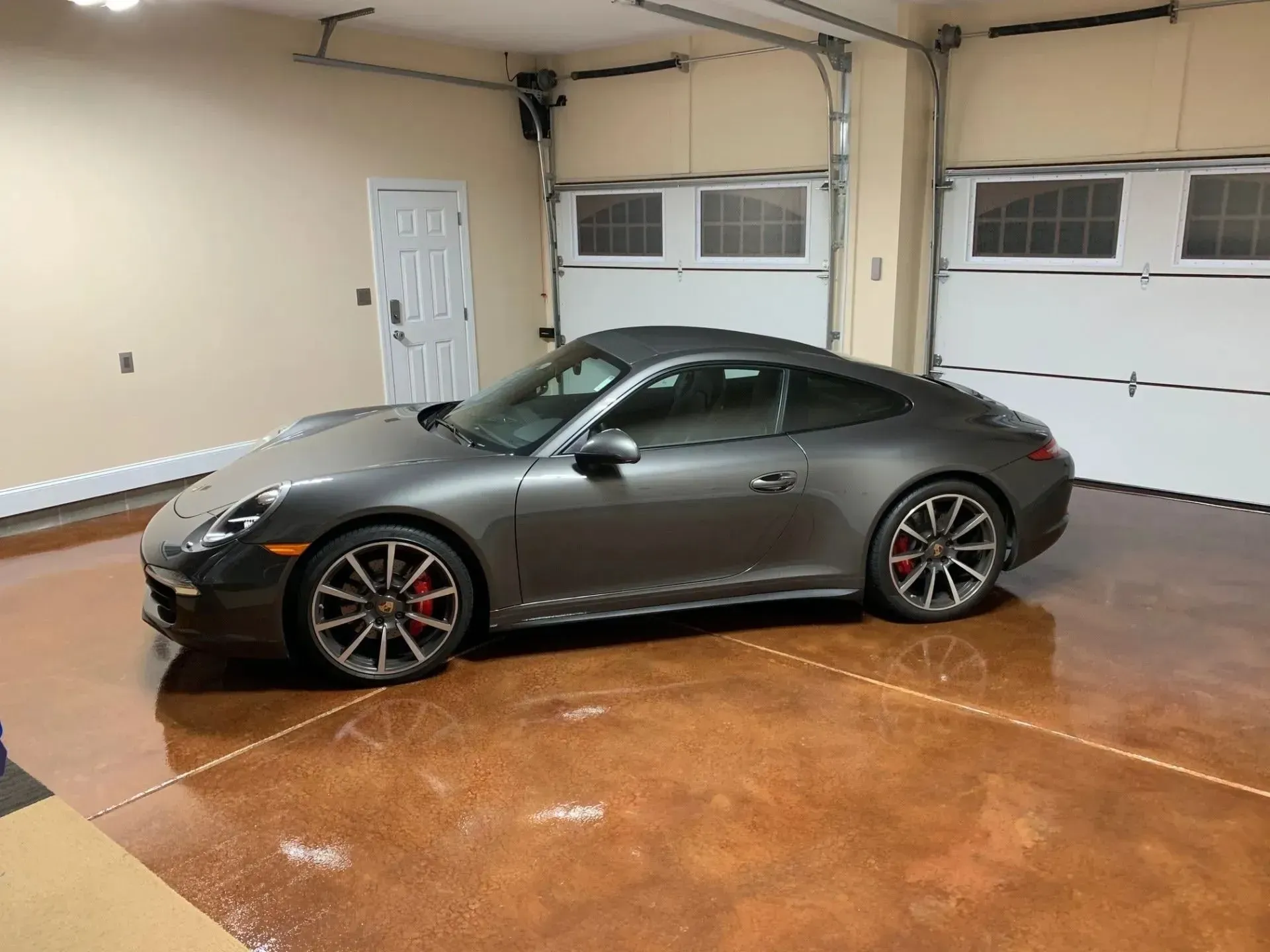 Gray Porsche sports car parked inside a garage with tan walls and stained concrete floor.