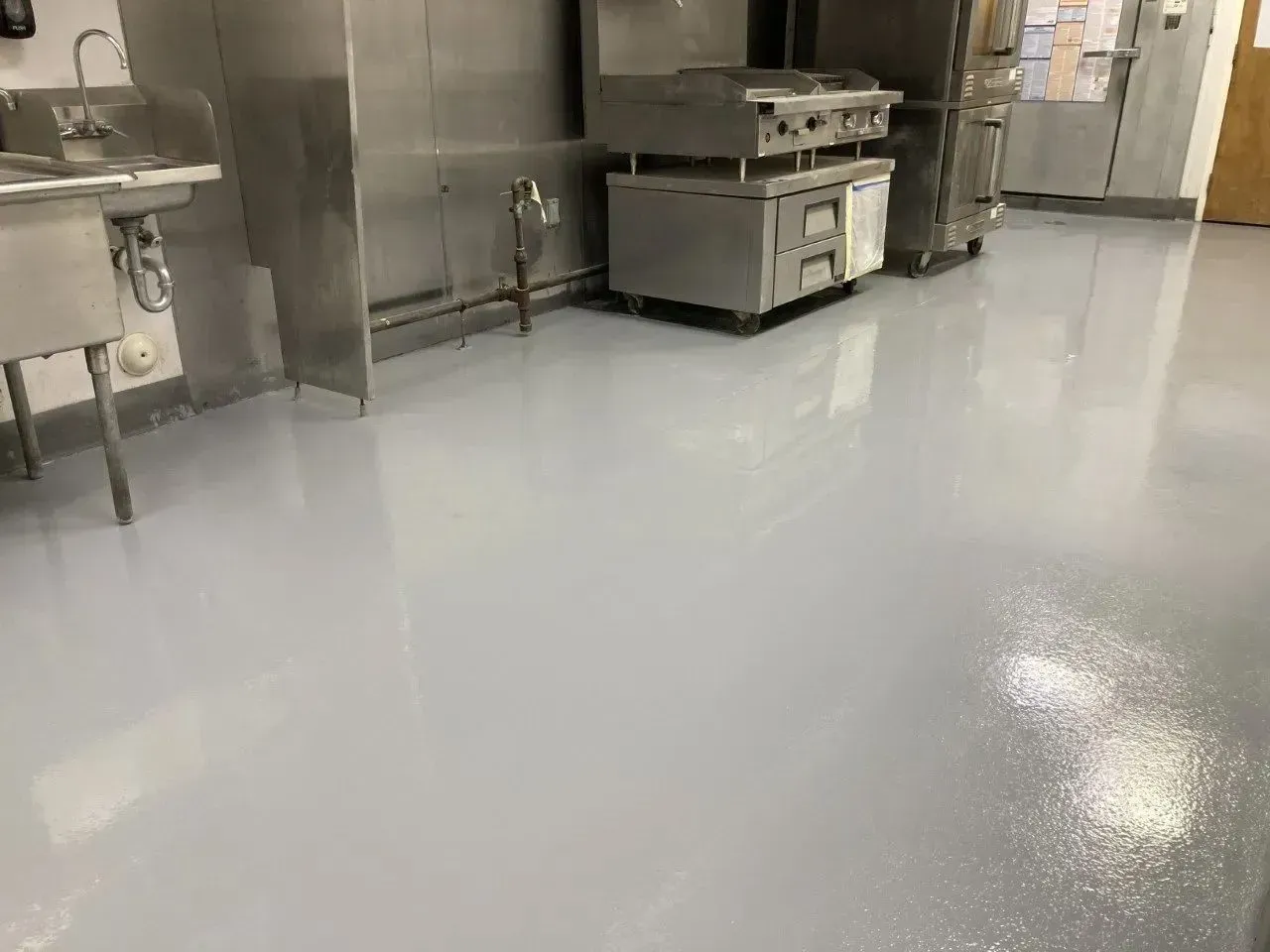 Commercial kitchen with shiny gray floor and stainless steel appliances.