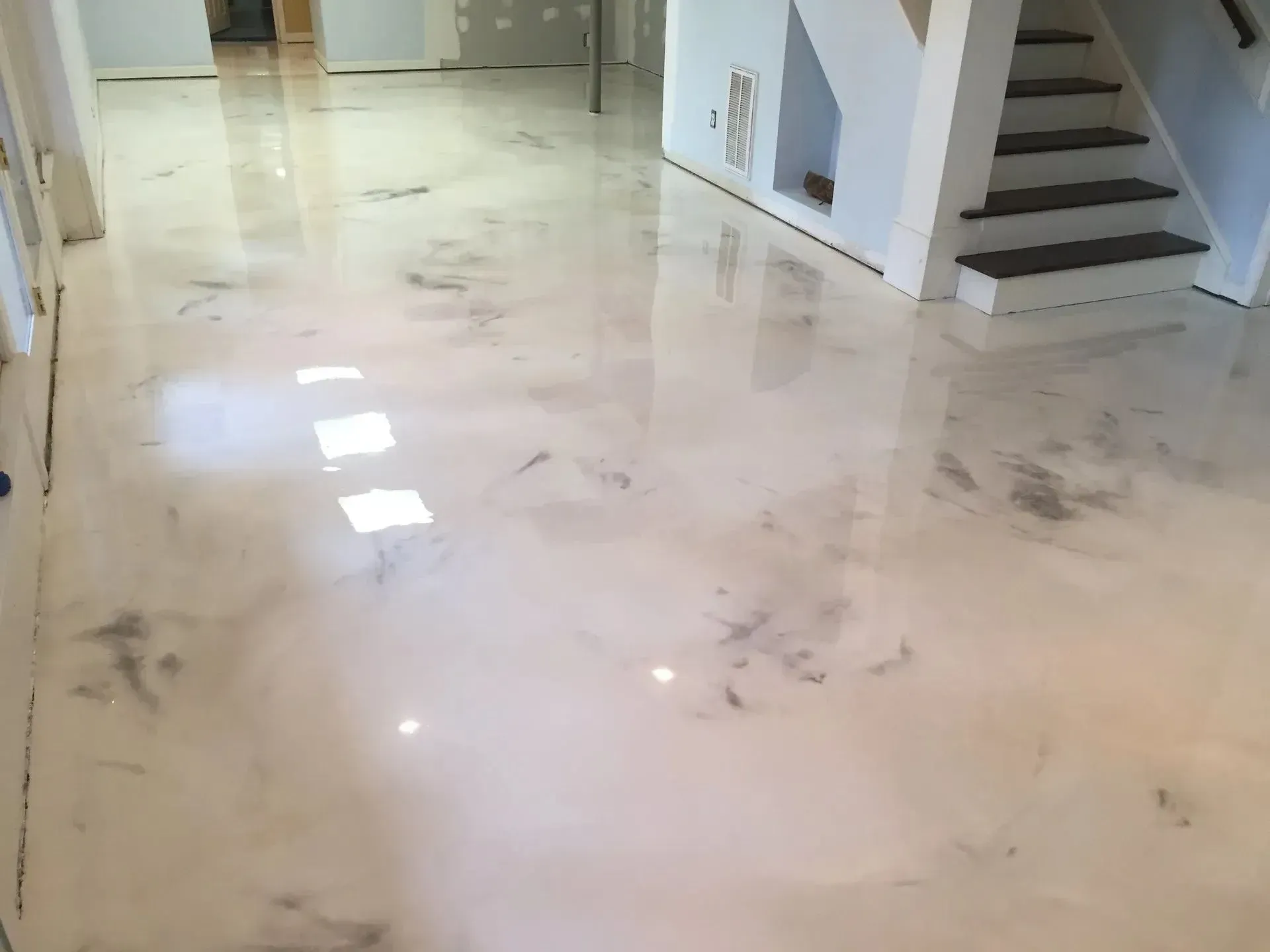 Shiny, metallic-looking epoxy floor in a room with white walls, stairs, and natural light.