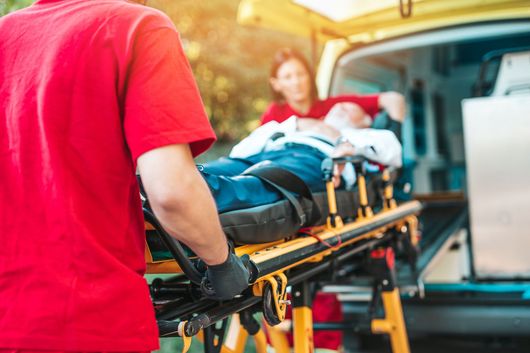 Emergency medical service at work. Paramedic is pulling stretcher with senior man with serious heart attack to the ambulance car. Help on the road. Drivers assistance concept.
