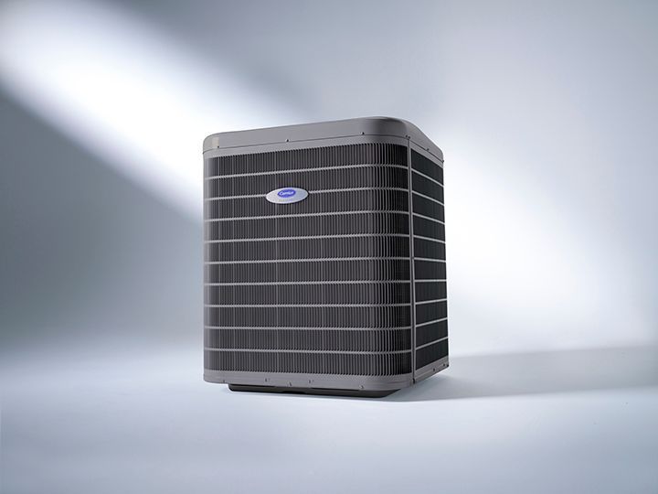 A grey Carrier outdoor air conditioning condenser unit set against a clean, light-colored studio background.
