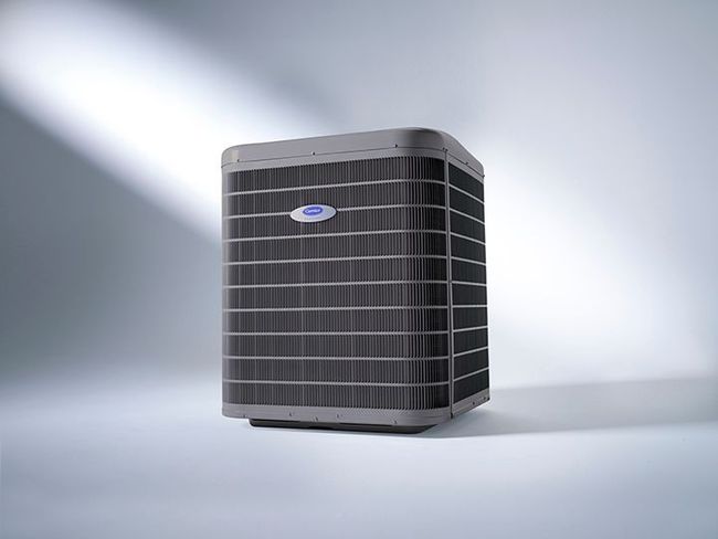 A grey Carrier outdoor air conditioning condenser unit set against a clean, light-colored studio background.