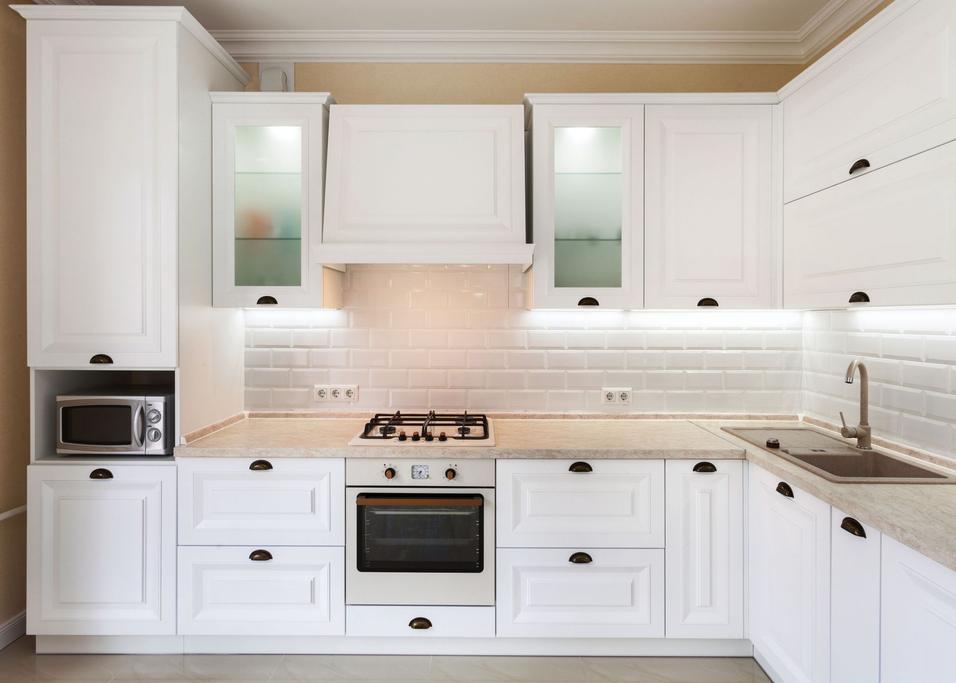 A kitchen with white cabinets , a stove , a sink , and a microwave.