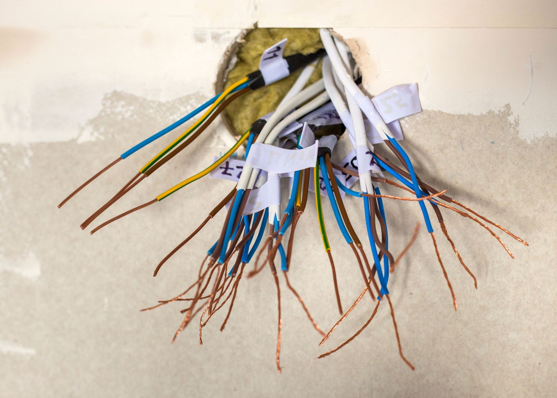 A bunch of wires are coming out of a hole in the wall.