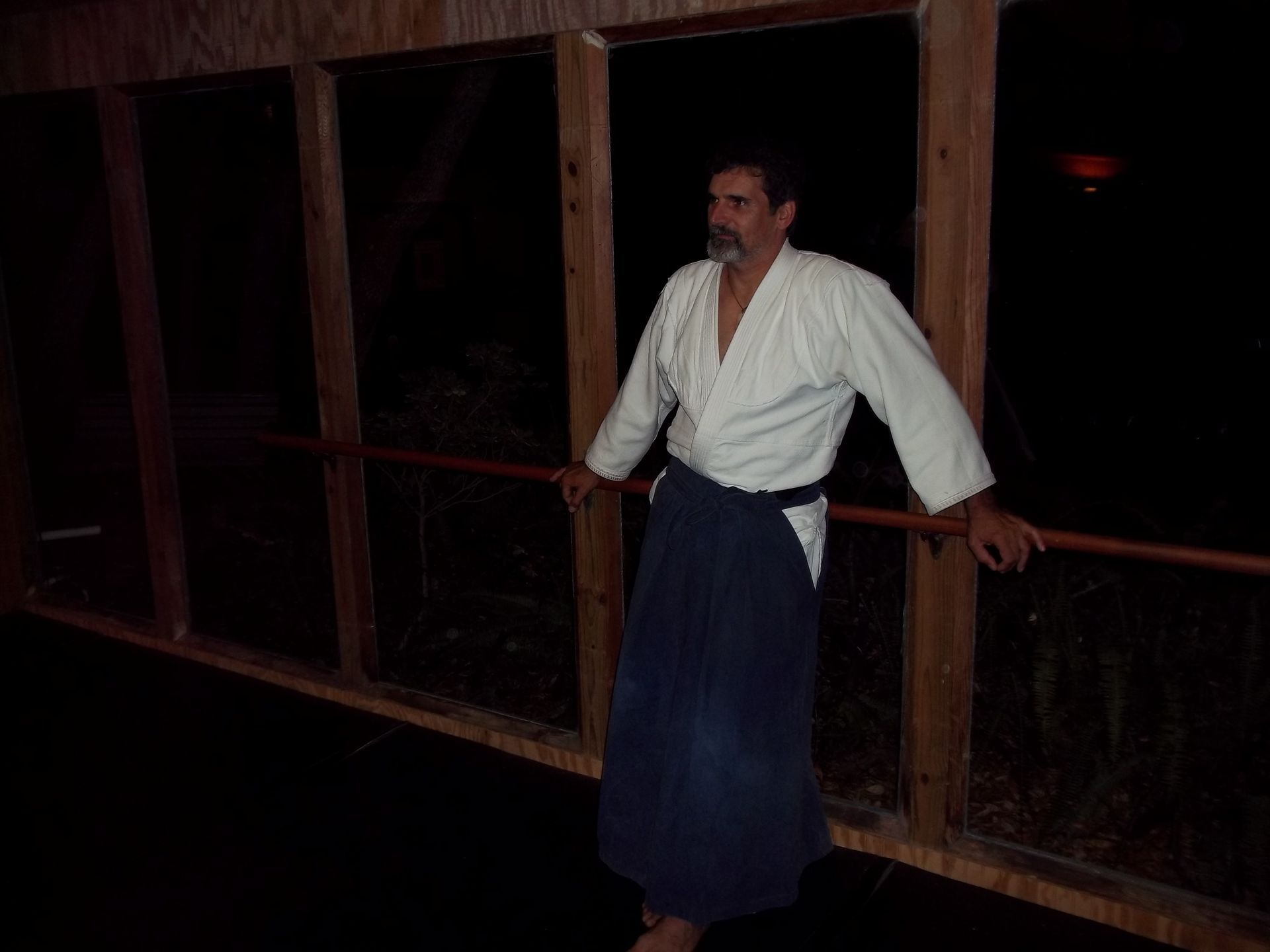 Man in white shirt and dark wrap leaning on a railing in a dimly lit wooden corridor