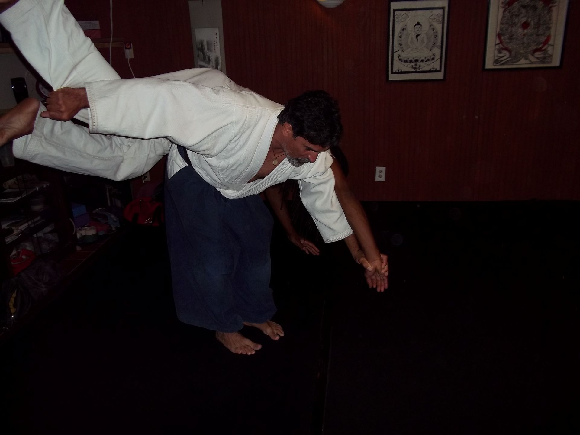 Person in a white gi is being thrown or lifted in a martial arts practice room.