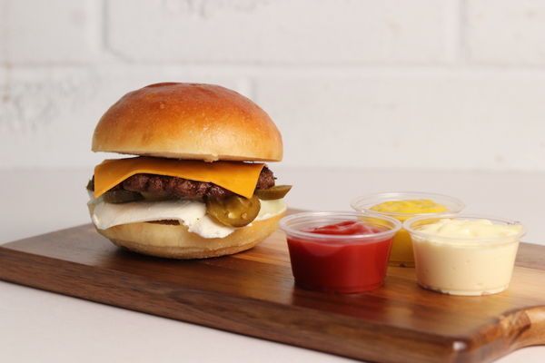 Cheeseburger with condiments on a wooden board.