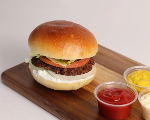 Burger with toppings, served on a wooden board with ketchup, mustard, and mayo.