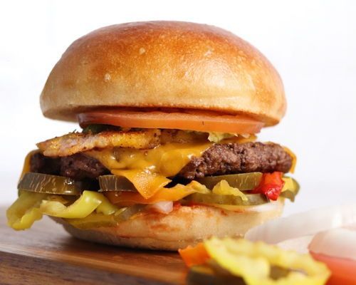Burger with patty, melted cheese, pickles, tomato, bacon, and bun.