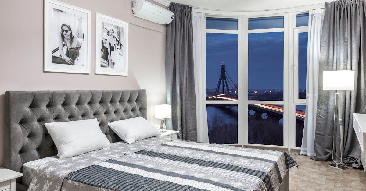 A bedroom with two beds , a large window and a view of the city.