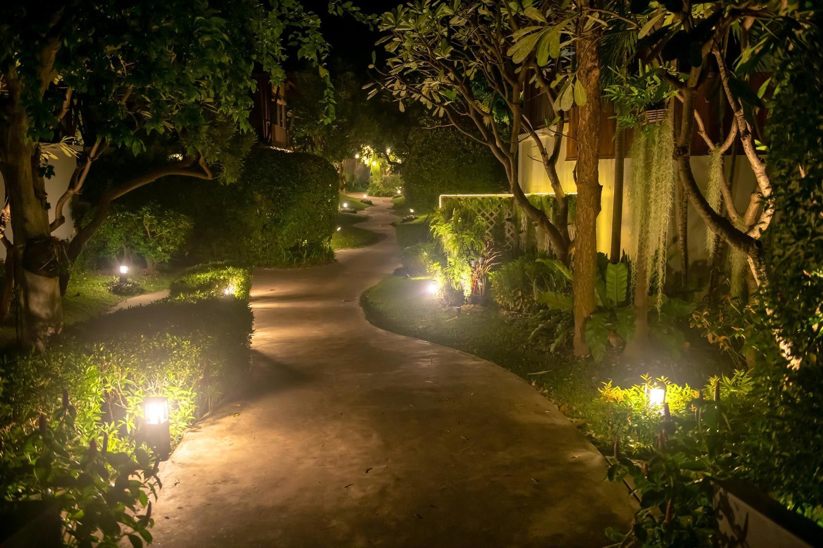 Curved garden walkway illuminated by low-voltage path lights and surrounded by lush greenery