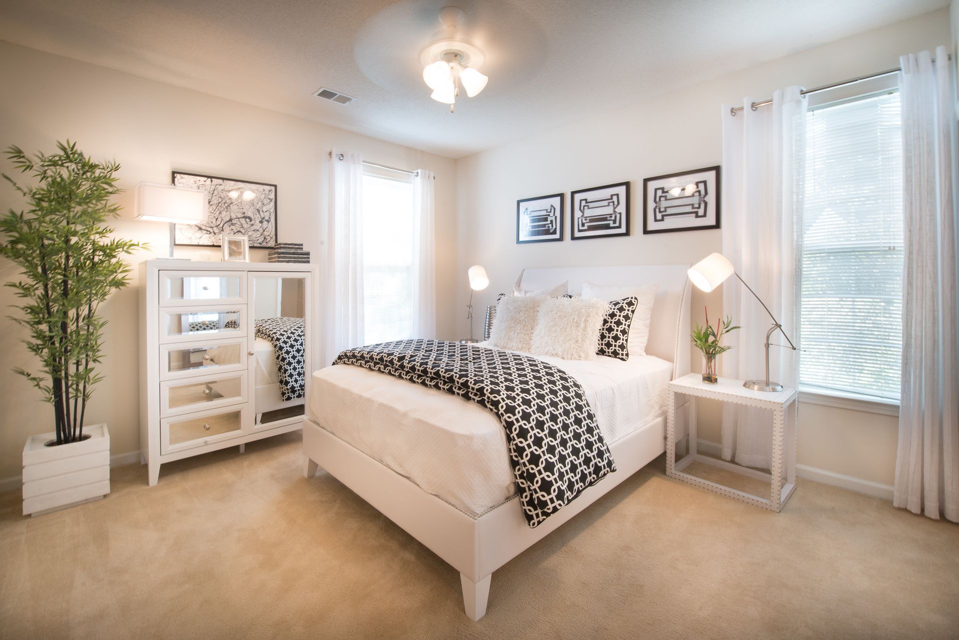 Bright bedroom with white bed, patterned bedding, wall art, lamps, and large windows with sheer curtains at Walden at Chatham Center Apartments in Savannah, GA