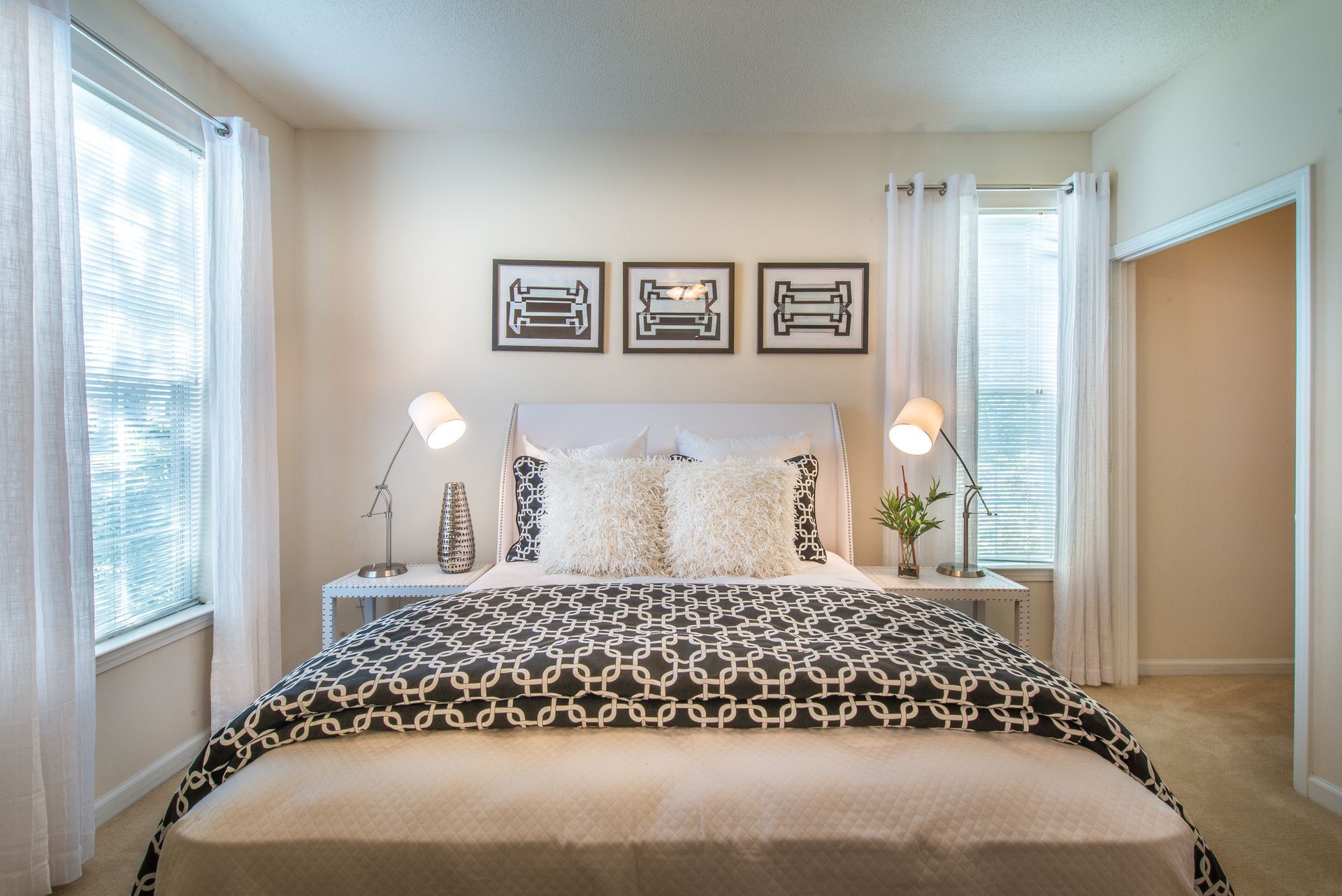 Bright bedroom with a neatly made bed, lamps, framed wall art, and windows with white curtains at Walden at Chatham Center Apartments in Savannah, GA