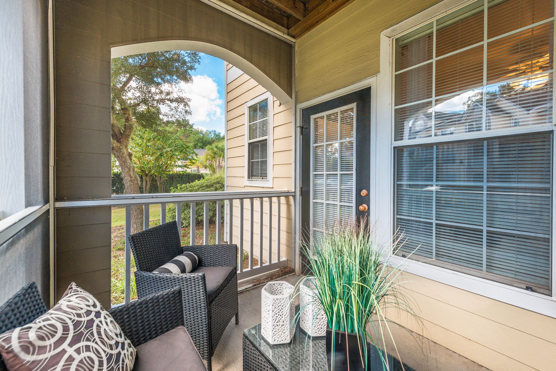 Covered apartment balcony with wicker chairs, potted plant, and view of trees and neighboring building at Walden at Chatham Center Apartments in Savannah, GA.