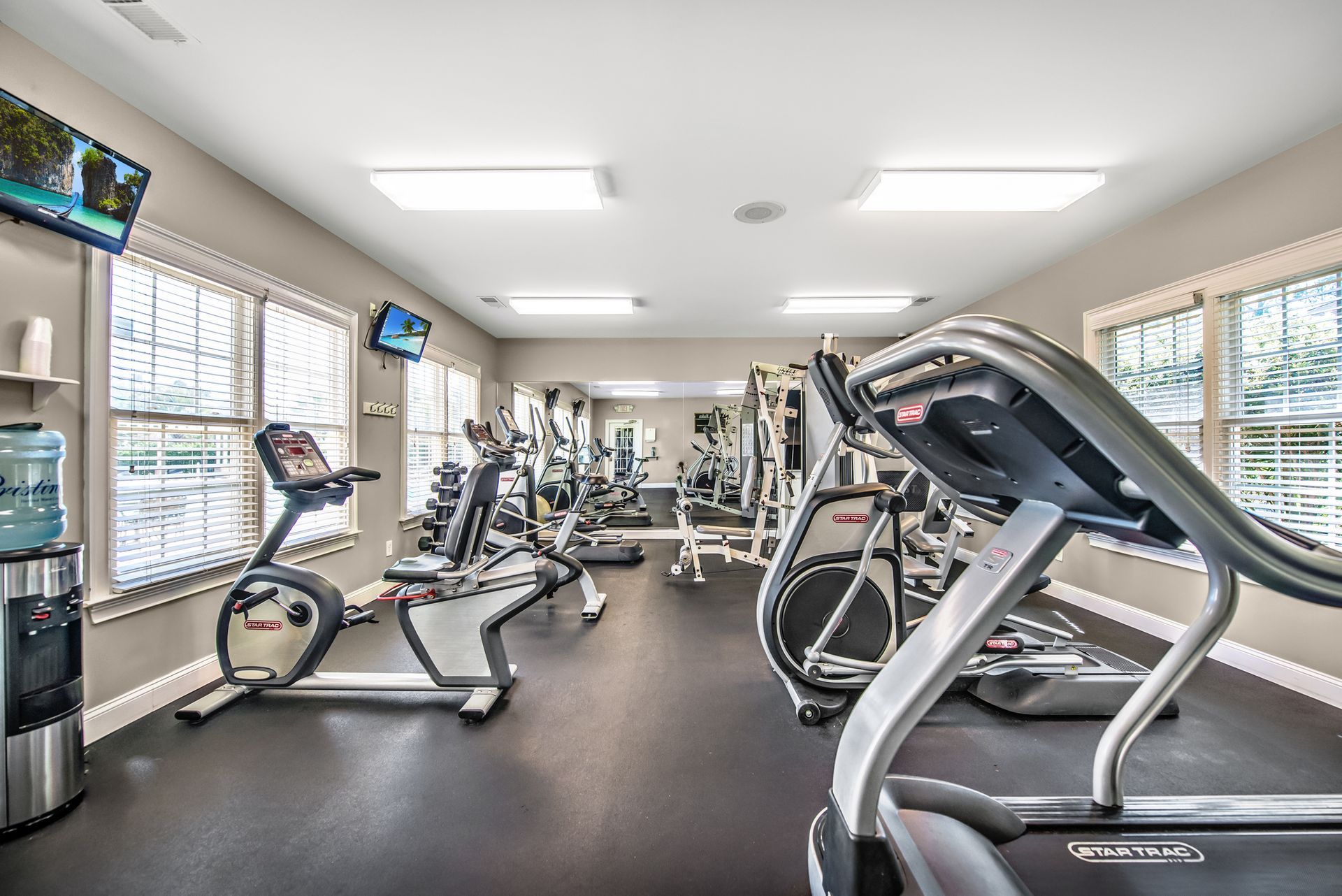 Bright gym with treadmills, stationary bikes, mirrors, and large windows at Walden at Chatham Center Apartments in Savannah, GA.