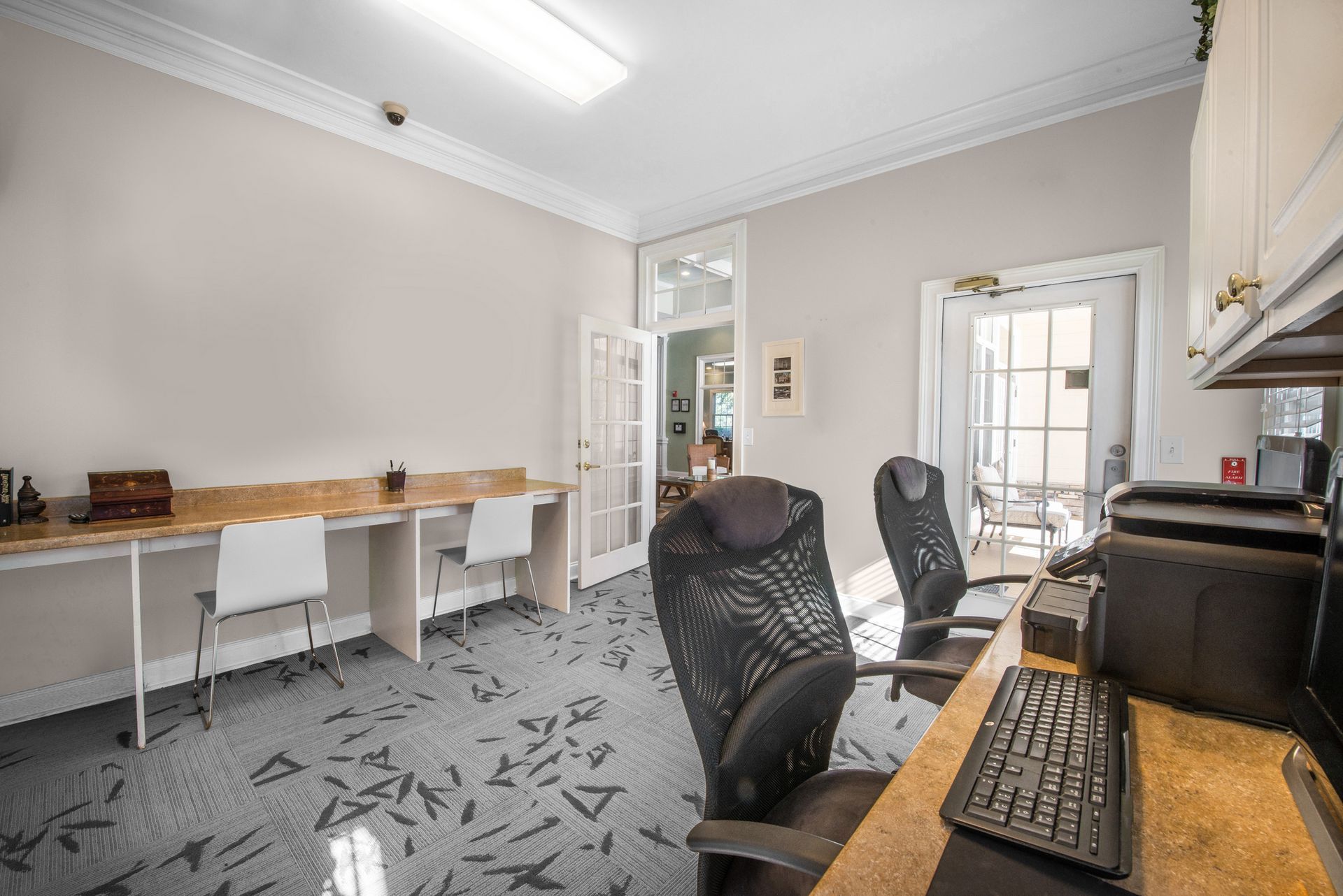 Office room with desks, computer chairs, and a printer on a desk near a glass door at Walden at Chatham Center Apartments in Savannah, GA.