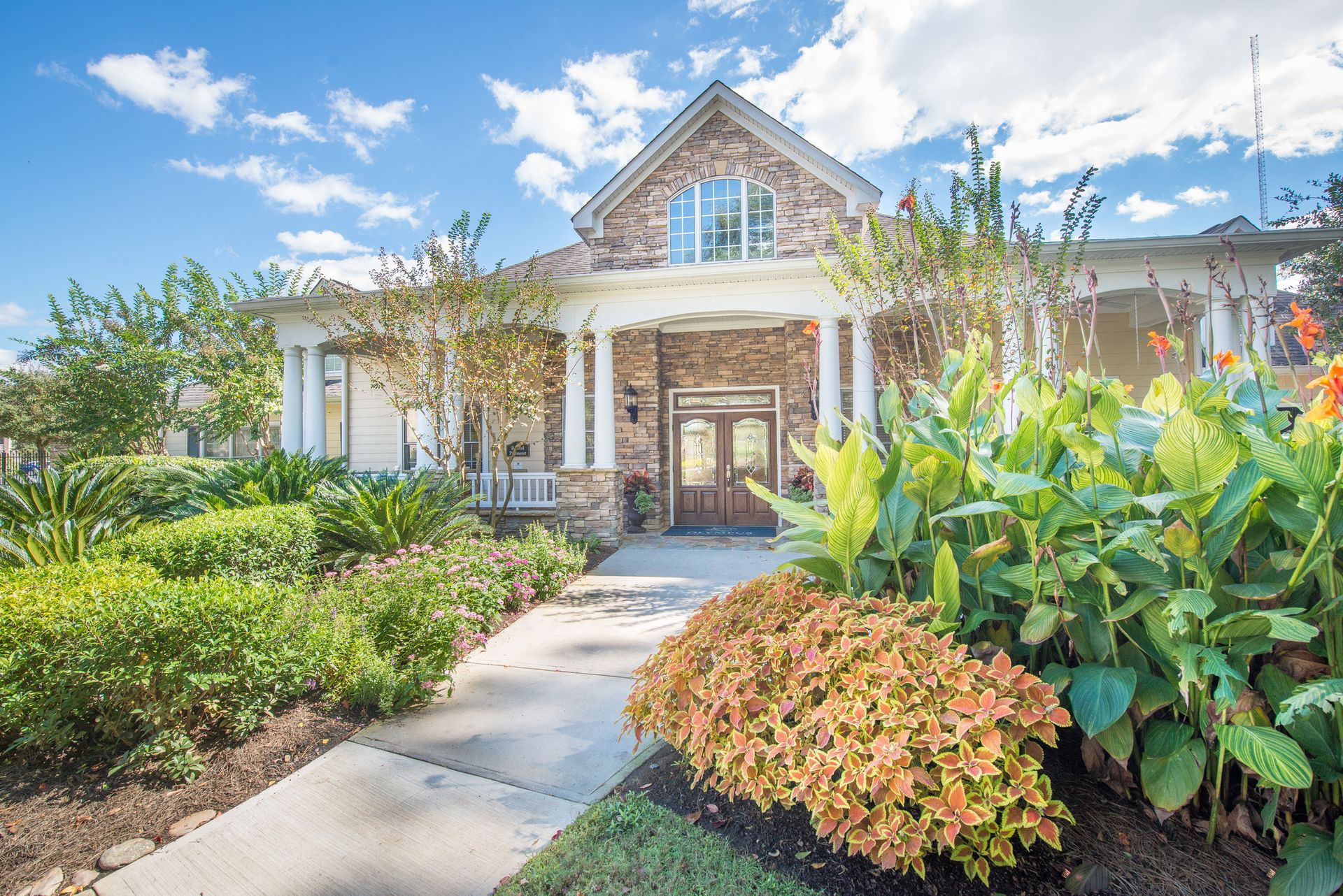Stone house with a front garden, walkway, and lush green and orange landscaping under a blue sky at Walden at Chatham Center Apartments in Savannah, GA.