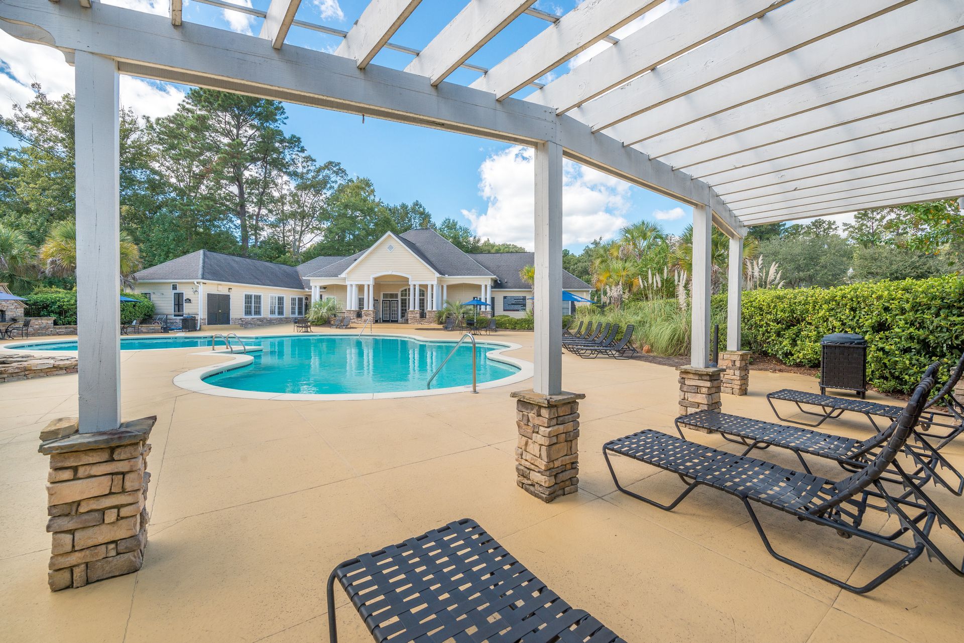 Covered patio with lounge chairs overlooking a blue backyard pool and house under a bright sky at Walden at Chatham Center Apartments in Savannah, GA.