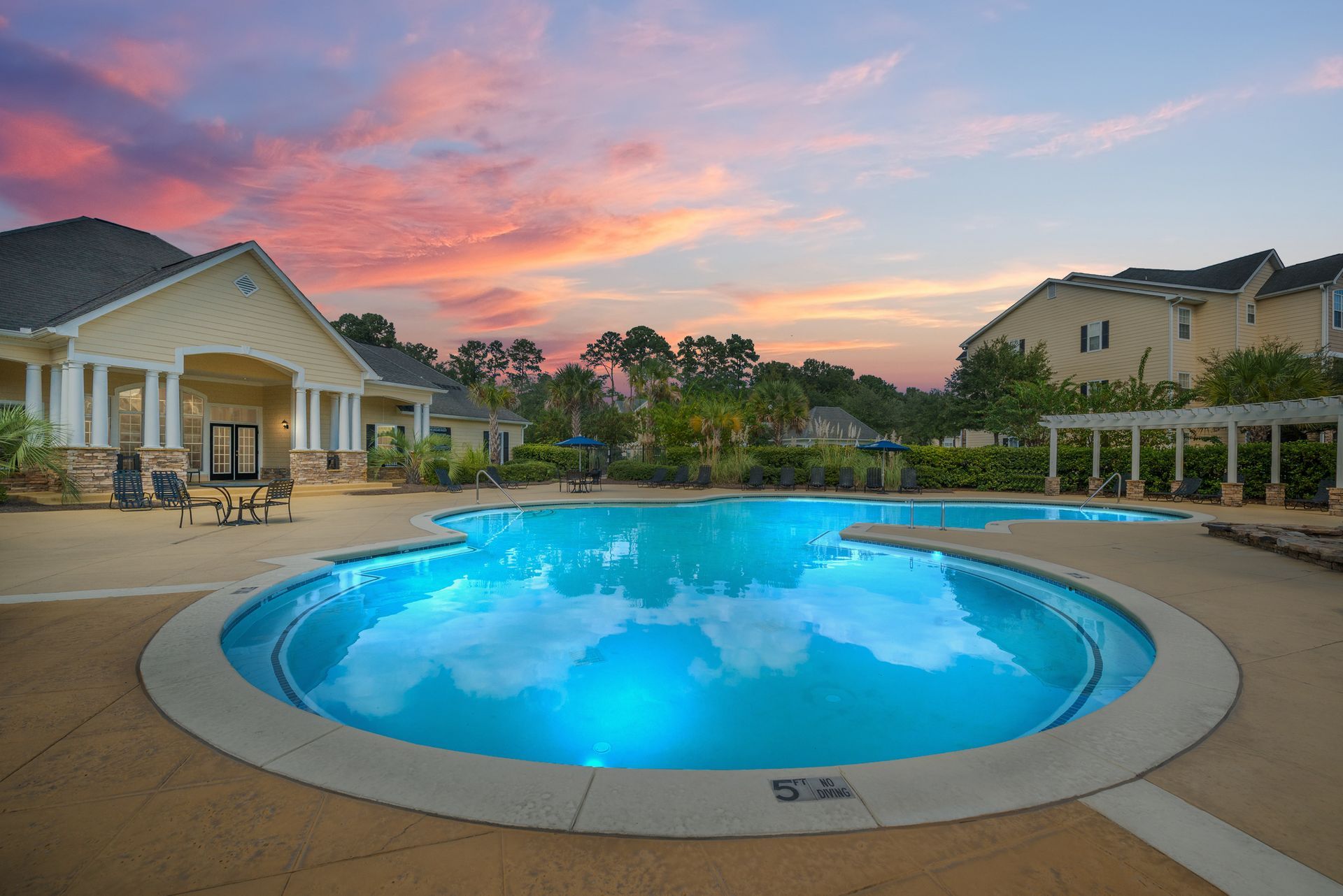 Backyard patio with a glowing blue pool at sunset, flanked by homes and a pergola at Walden at Chatham Center Apartments in Savannah, GA.