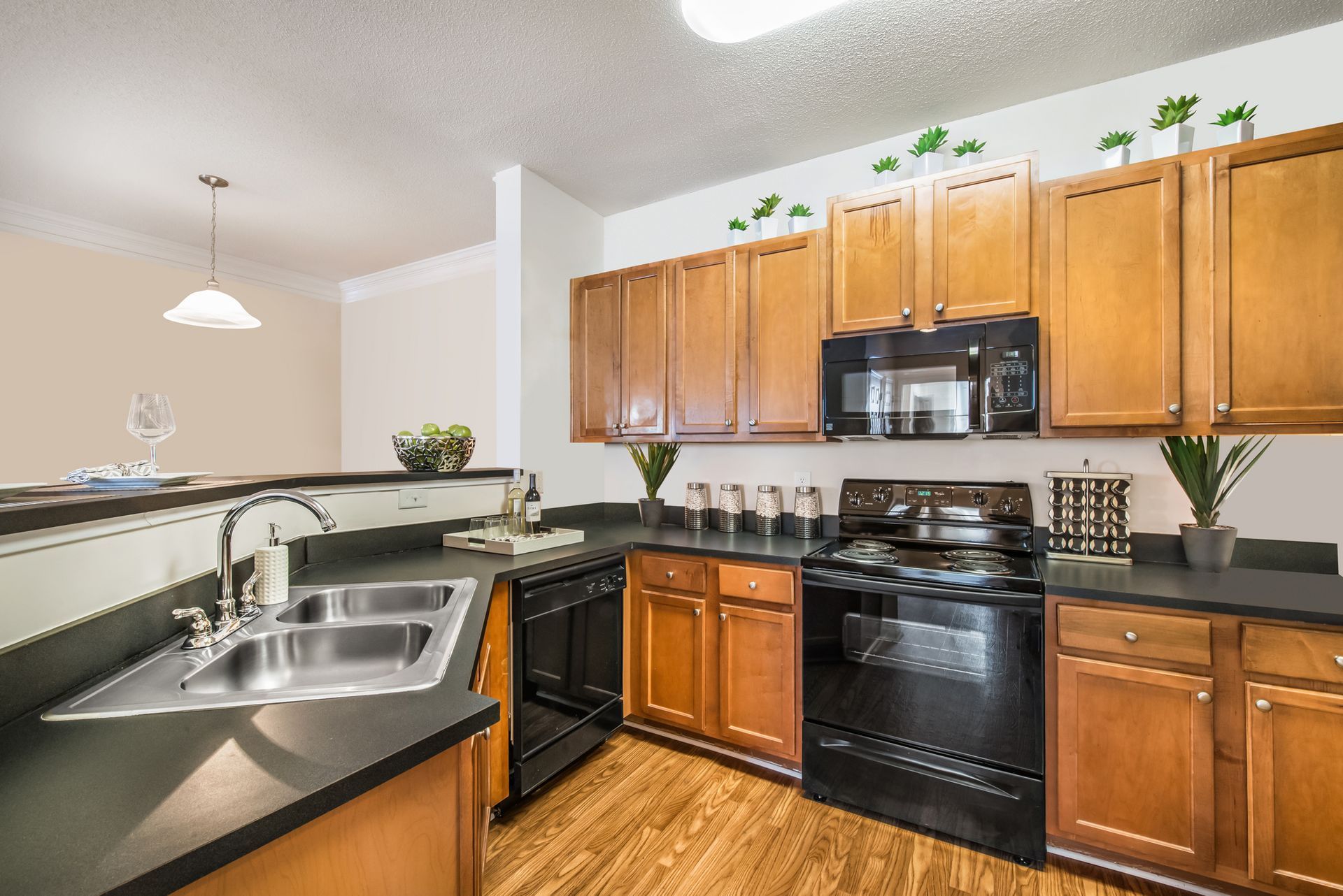 Modern kitchen with wooden cabinets, black appliances, and a granite countertop with a stainless-steel sink at Walden at Chatham Center Apartments in Savannah, GA
