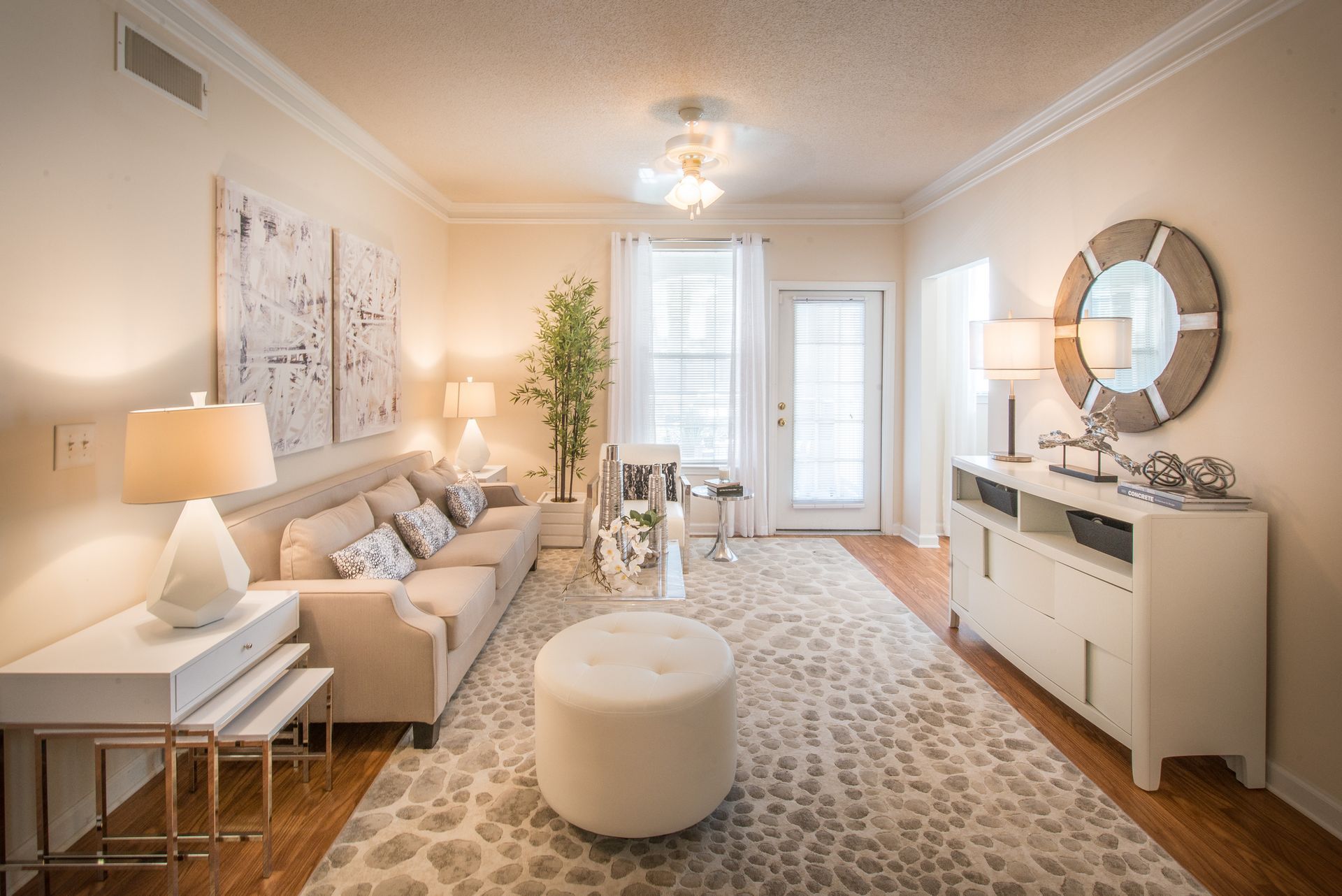Bright living room with beige sofa, patterned rug, white console, round mirror, and glass door to balcony at Walden at Chatham Center Apartments in Savannah, GA