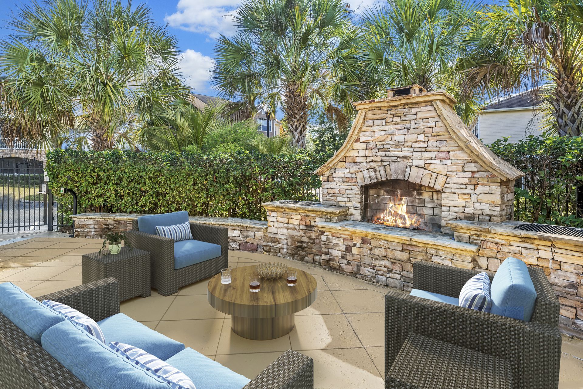 Backyard patio with wicker seating around a fire pit and a stone outdoor fireplace under a blue sky at Walden at Chatham Center Apartments in Savannah, GA.