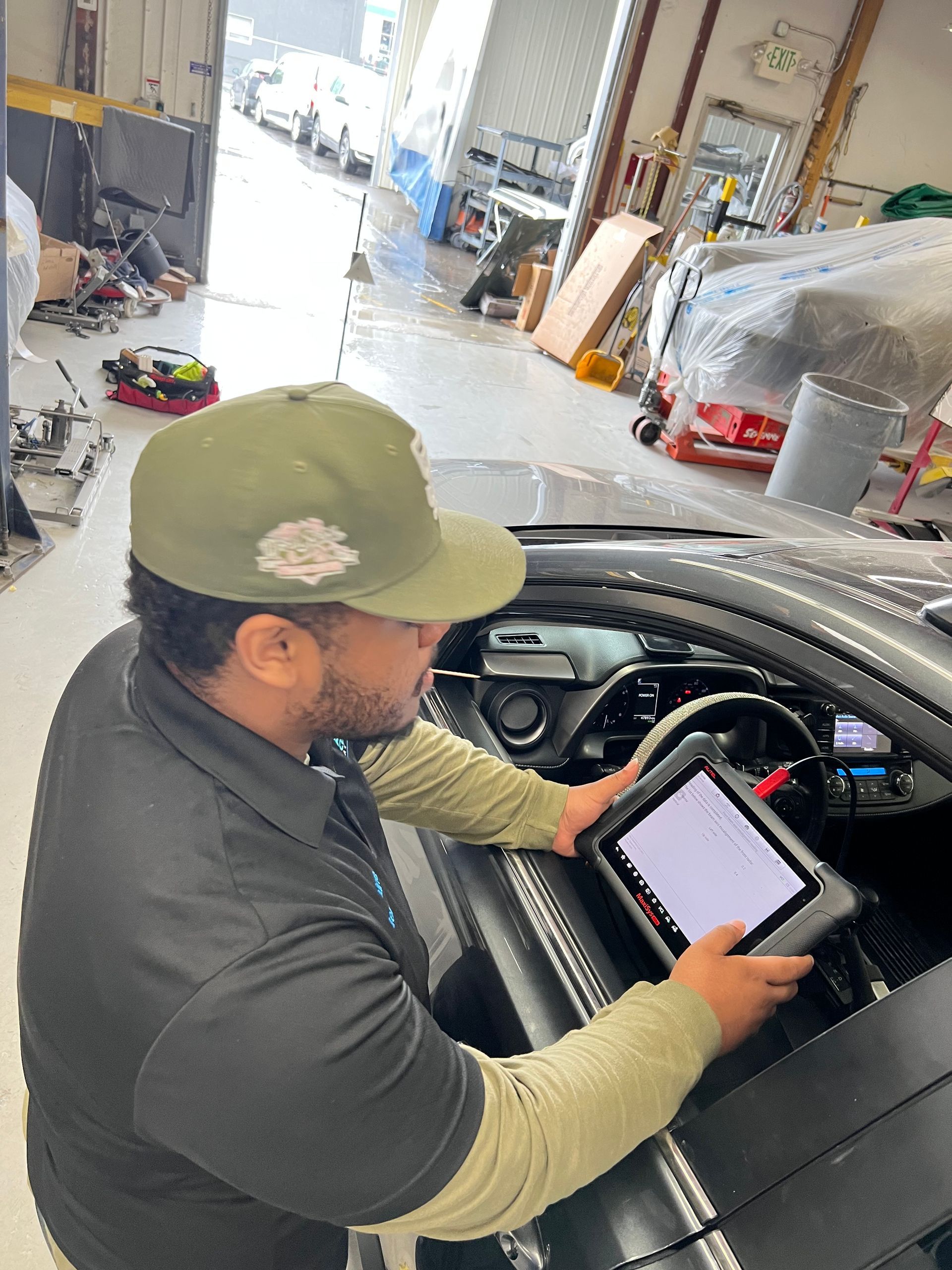 A man is working on a car in a garage using a tablet.