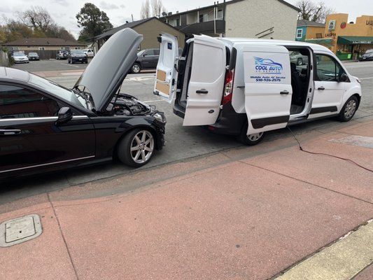 A black car is parked next to a white van with the doors open.