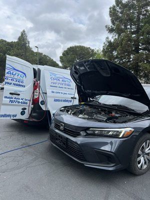 A car with its hood open is parked next to a van.